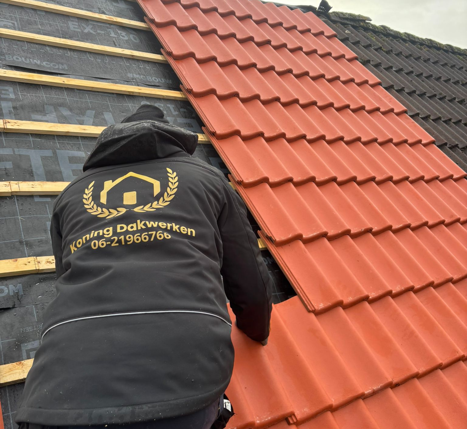 Dakdekker installeert nieuwe oranje dakpannen op dak.